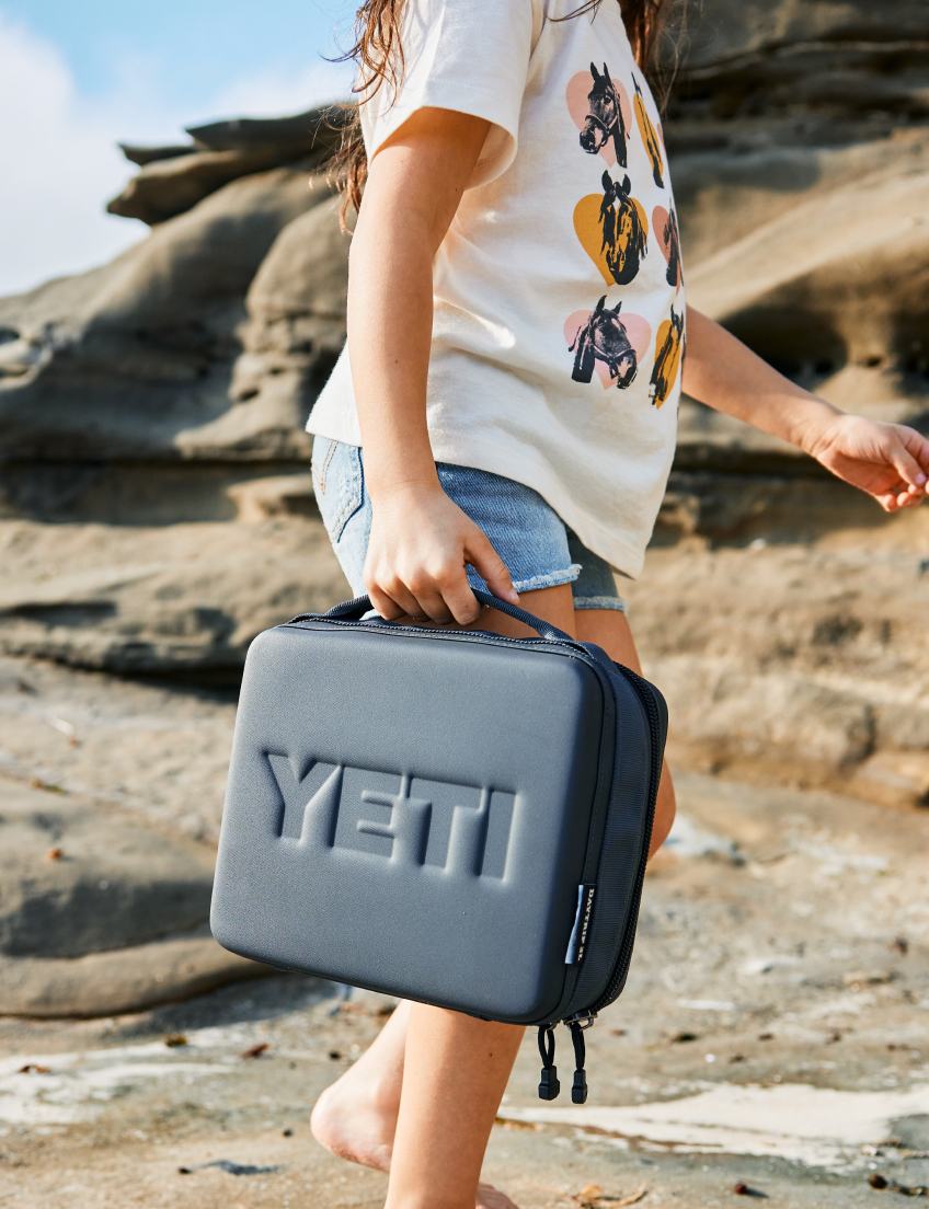 Person holding a YETI branded daytrip cooler on a rocky beach