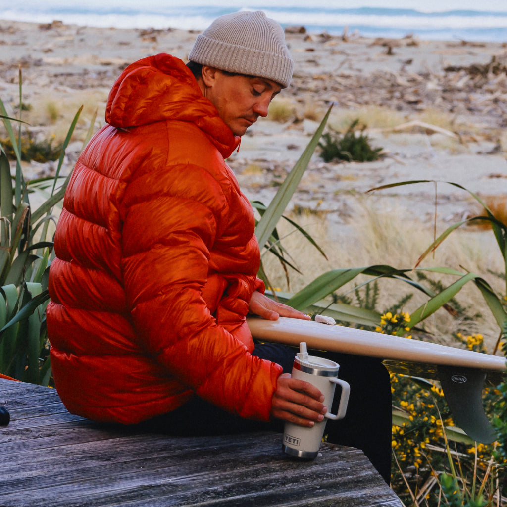 Person in a red puffer jacket sitting outdoors with a scenic background with a Rambler® Travel Straw Mug