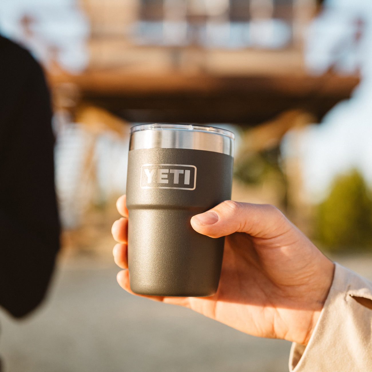 Hand holding a black insulated cup with 'YETI' branding outdoors.