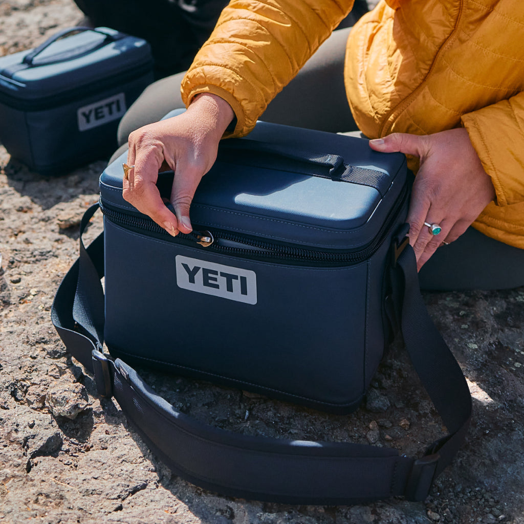 Person opening a YETI cooler on a rocky surface