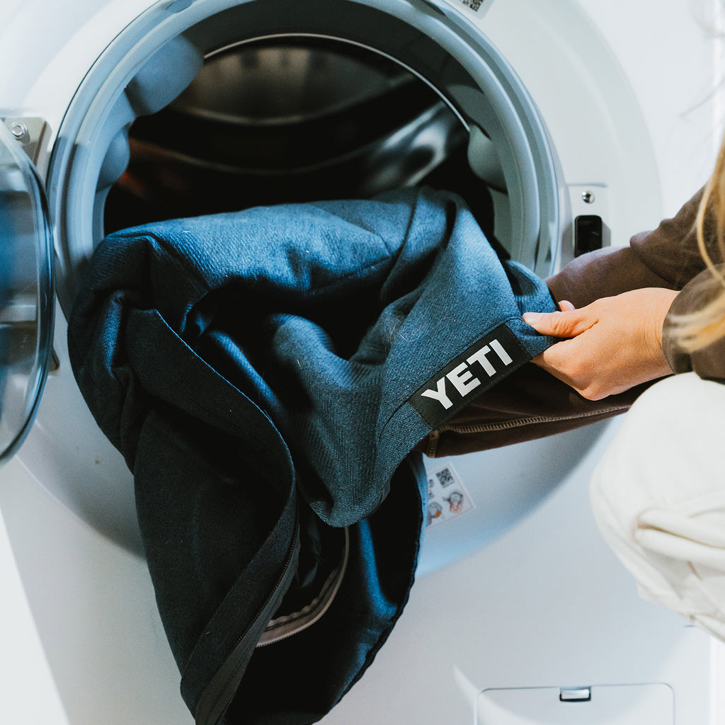 A person putting the cover from a YETI Boomer Dog Bed into a washing machine