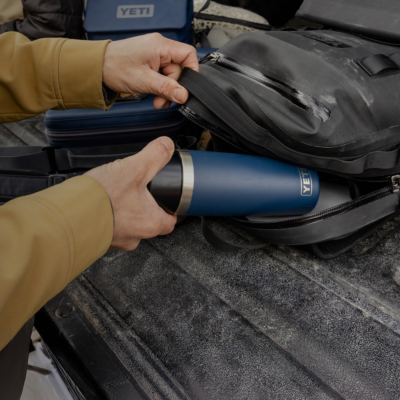Person placing a YETI branded tumbler into a backpack on a vehicle's bed.
